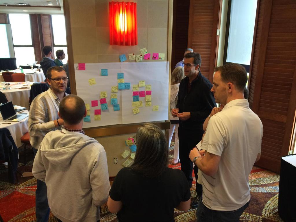 Small workshop group collaborating around a board covered with sticky notes during a design system planning session.